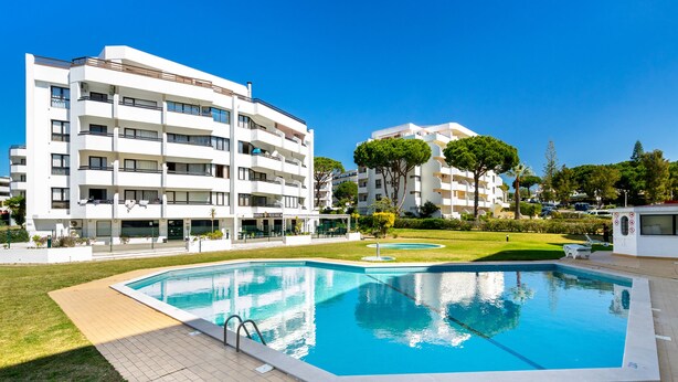 A modern apartment building with a swimming pool, surrounded by well-maintained lawns and trees.