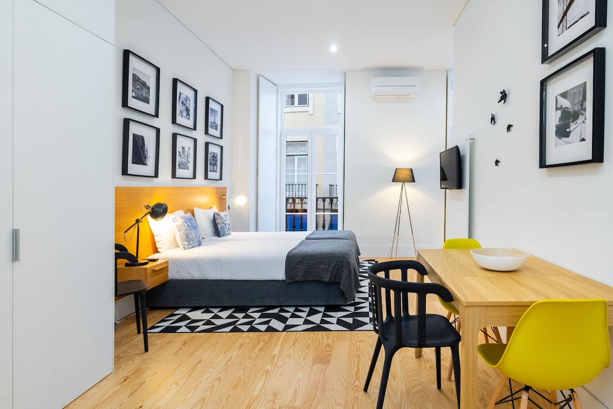 Ein kleines Hotelzimmer mit Bett, Nachttisch, Lampe und einem Essbereich mit Stühlen und Tisch.