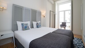 Quarto moderno com uma cama grande, duas mesas de cabeceira, um abajur e vista para a varanda.