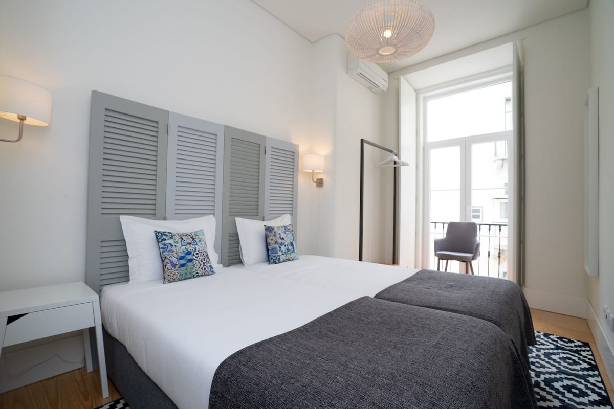 Ein modernes Schlafzimmer mit einem großen Bett, zwei Nachttischen, einer Stehlampe und Blick auf den Balkon.
