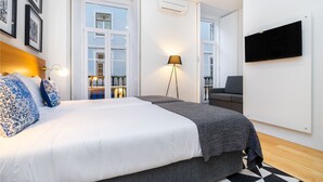 Quarto moderno com uma cama grande, uma TV na parede e uma varanda com vista para a cidade.