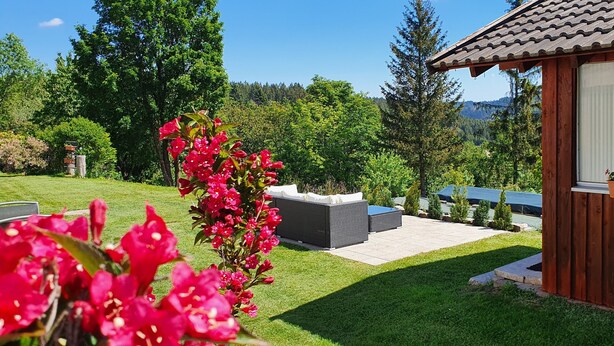 Un espace patio aménagé avec du mobilier d’extérieur, une terrasse en bois et une vue sur un paysage boisé.