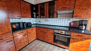 Une cuisine avec des meubles de rangement en bois, un plan de travail noir, une cuisinière et une machine à café.