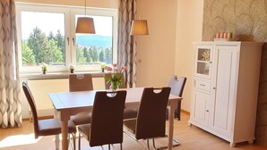 Un coin repas comprenant une table, des chaises, un buffet et une vue sur les arbres et les montagnes par la fenêtre.