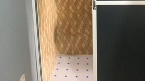 Un baño con pared de baldosas estampadas, una puerta blanca y un pequeño estante con una botella.