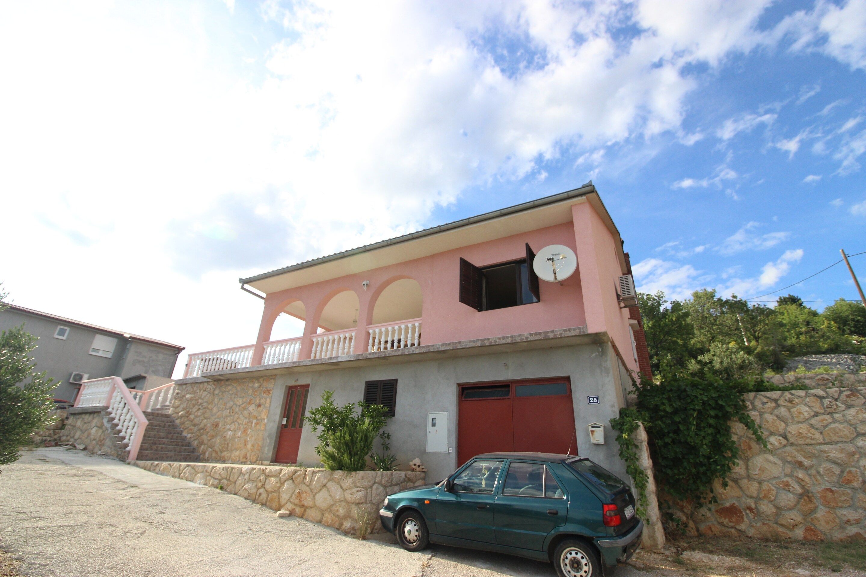 A two-story building with a balcony, a satellite dish, and a parked car.