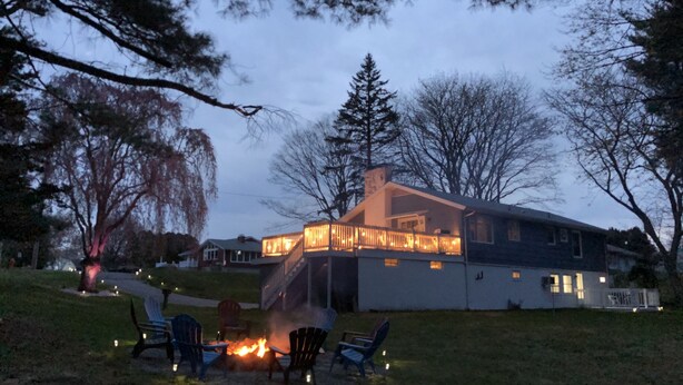 A house with a fire pit in the yard, surrounded by chairs.