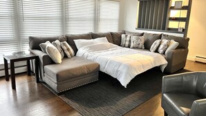 A modern living room with a sectional sofa, a small table, and a large window with blinds.