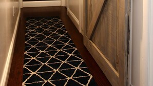A hallway with a wooden floor, a geometric patterned rug, a wooden wall with a hanging anchor decoration, and a barn-style door.