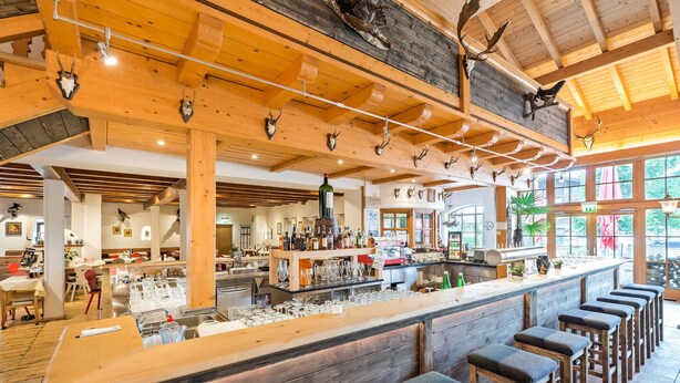A rustic bar area with wooden beams, antler decorations, and bar stools. - Family suite with 2 bedrooms 45 sqm (Inzell)