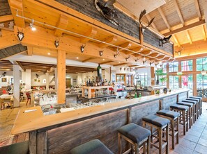 Un coin bar au style rustique, avec des poutres en bois, des décorations en forme de bois de cerf et des tabourets de bar.