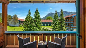 A wooden balcony with wicker chairs and a table, overlooking a mountain landscape with buildings. - Family suite with 2 bedrooms 45 sqm (Inzell)
