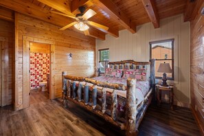 Une chambre dans une cabane en bois, avec un lit, un ventilateur de plafond, une fenêtre et une porte en bois.