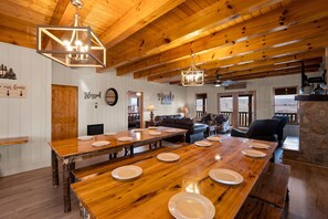 Une salle à manger spacieuse avec une longue table en bois dressée pour le repas, un salon confortable doté d’une cheminée et un mur en pierre qui apporte une touche d’originalité.
