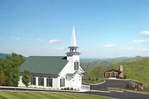 Une église blanche, dotée d’un clocher et d’un petit bâtiment attenant, le tout entouré de collines verdoyantes.