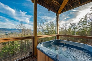 Un jacuzzi con cubierta de madera y vistas a montañas y árboles.