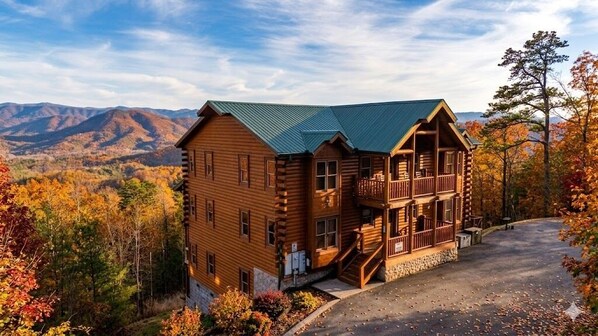 Un chalet en rondins doté d’un balcon, entouré d’un feuillage automnal et de montagnes.