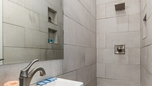 A bathroom with a white sink, a mirror, and a shower area with tiled walls and floor. - Cozy Suite in Downtown Charleston with HEATED POOL (Charleston)