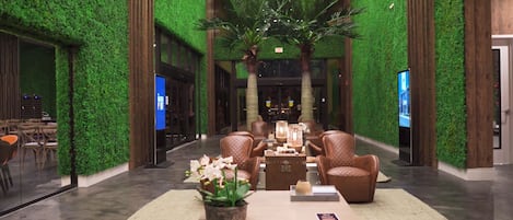 Un vestíbulo con paredes verdes, sillones de cuero, una mesa de centro y una palmera grande.