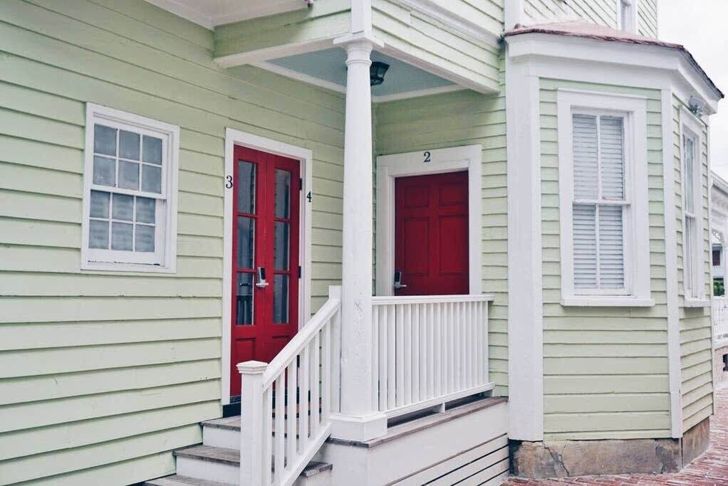 Une maison verte avec une porte rouge et une balustrade blanche sur le porche.