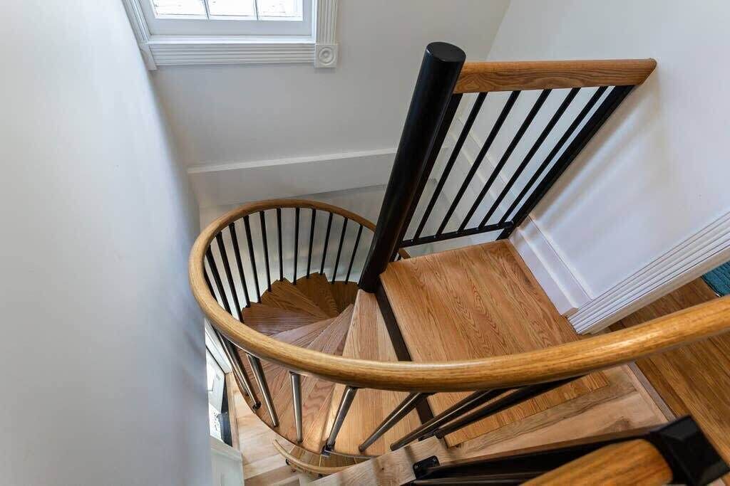 A wooden spiral staircase with black metal railings and a white wall.