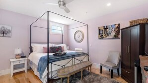 Un dormitorio con una cama con dosel, un banco, una silla, un armario y un ventilador de techo.