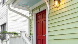 Una casa con puerta roja, cerca blanca enrejada y fachada verde.