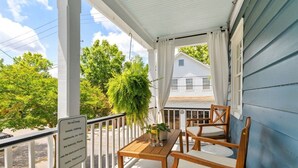 A covered porch with a wooden table and chairs, a potted plant, and a sign advising against hanging items from the railing. - Beautifully Restored  Downtown Apartment (Charleston)