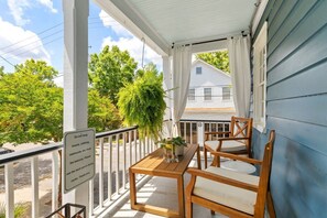 A wooden porch with a table and chairs, a sign advising against hanging items, and a view of a house and trees.