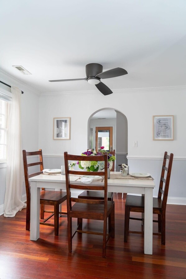 A dining room with a white table, four wooden chairs, a ceiling fan, and a mirror on the wall.