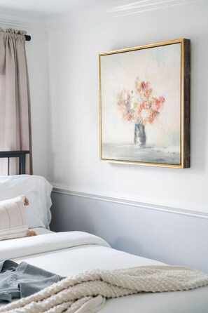 A bedroom with a bed, a painting of flowers, and a window with curtains.