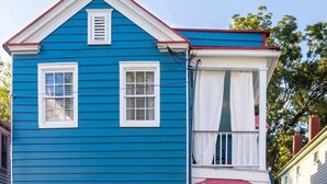 A two-story blue house with a white door marked '149' and a small porch with a red awning. - Beautifully Restored  Downtown Apartment (Charleston)