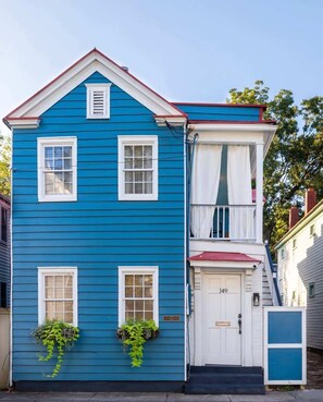 A two-story blue house with white trim, a front door labeled "149", and a small porch with a red awning.