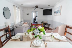 A dining area with a table set for four, a ceiling fan, and a view into the adjacent living room.