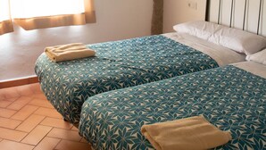 A room with two beds, wooden beams on the ceiling, a window with curtains, and a tiled floor. - Complejo Rural Puente Romano (Orgaz)