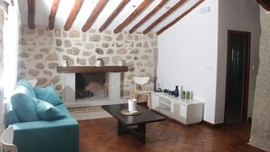 A cozy living room with a stone fireplace, wooden beams, a sofa, and a coffee table. - Complejo Rural Puente Romano (Orgaz)