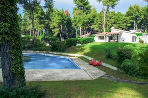 Una piscina rodeada de exuberante vegetación y un edificio blanco con tejado de tejas.