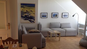 Ein gemütliches Wohnzimmer mit einem Holzesstisch, einem grauen Sofa und einem Bild an der Wand.