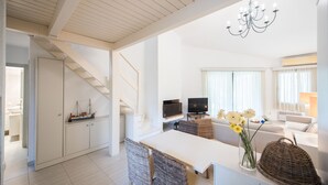 Una cocina moderna con armarios blancos, un comedor con sillas de mimbre y una escalera que sube a otro nivel.