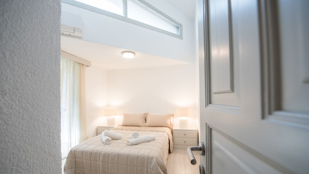 Un dormitorio con cama, lámparas de noche, una ventana y una puerta.