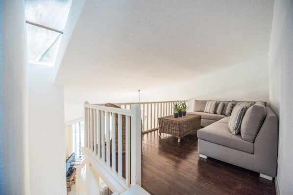 A spacious living area with a high ceiling, a wooden floor, a beige sofa, and a wicker coffee table. - Villa Armonia by halu! Villas (Kassandra)