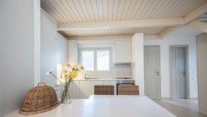 Una cocina moderna con armarios blancos, una isla central con sillas de mimbre y un jarrón con flores.