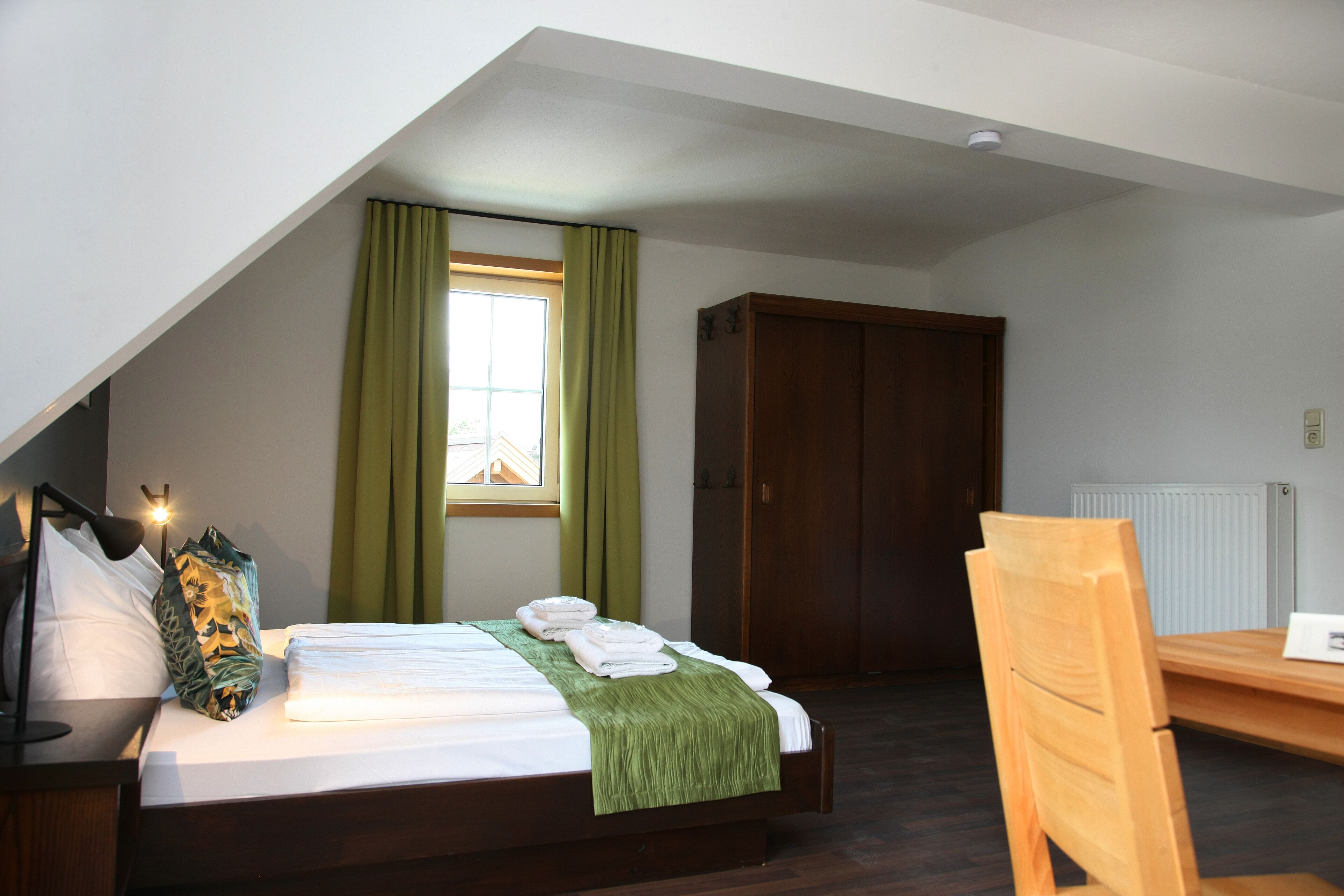 Ein Schlafzimmer mit einem Bett, einem Holzbett, einem Schreibtisch, einem Fenster mit Vorhängen und einem Kleiderschrank.