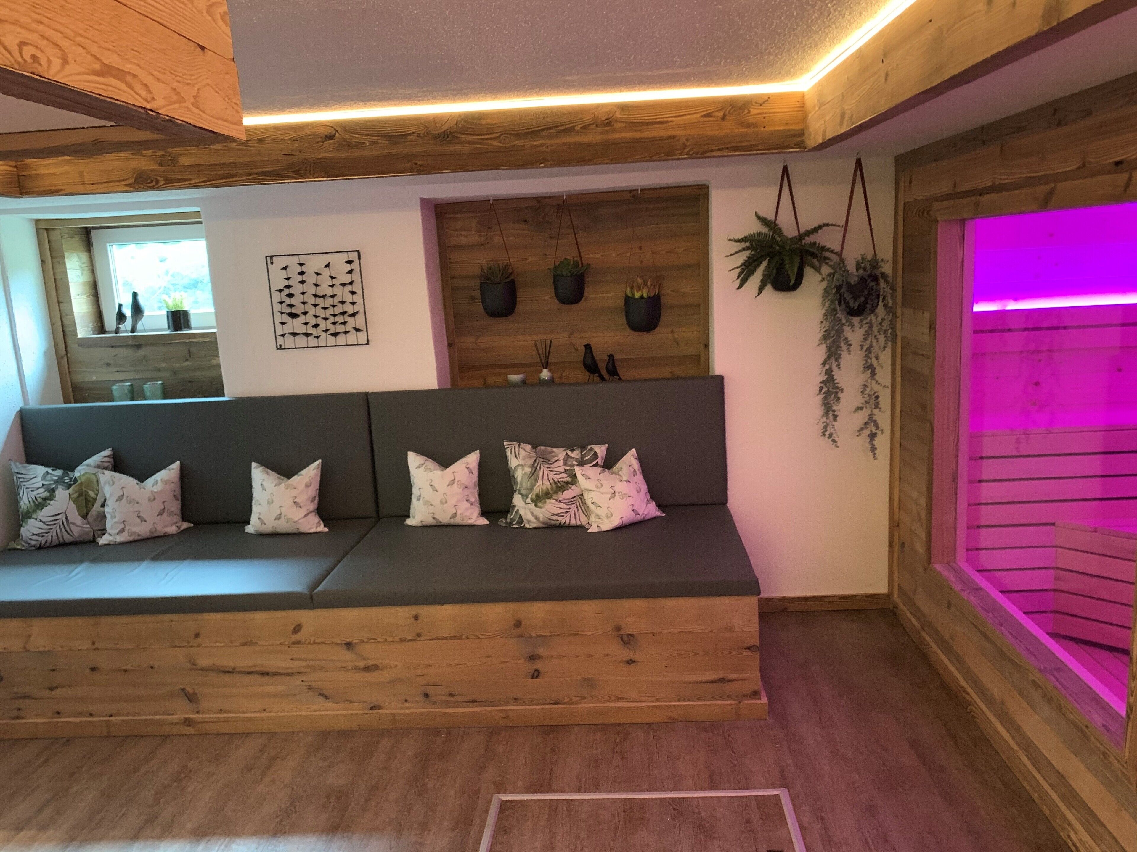 Un moderno salón con un banco de madera, un jarrón de plantas en la pared y un rincón iluminado en morado.