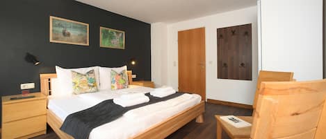 Un dormitorio moderno con una cama grande, mesitas de noche de madera, una silla de madera y dos cuadros en la pared.