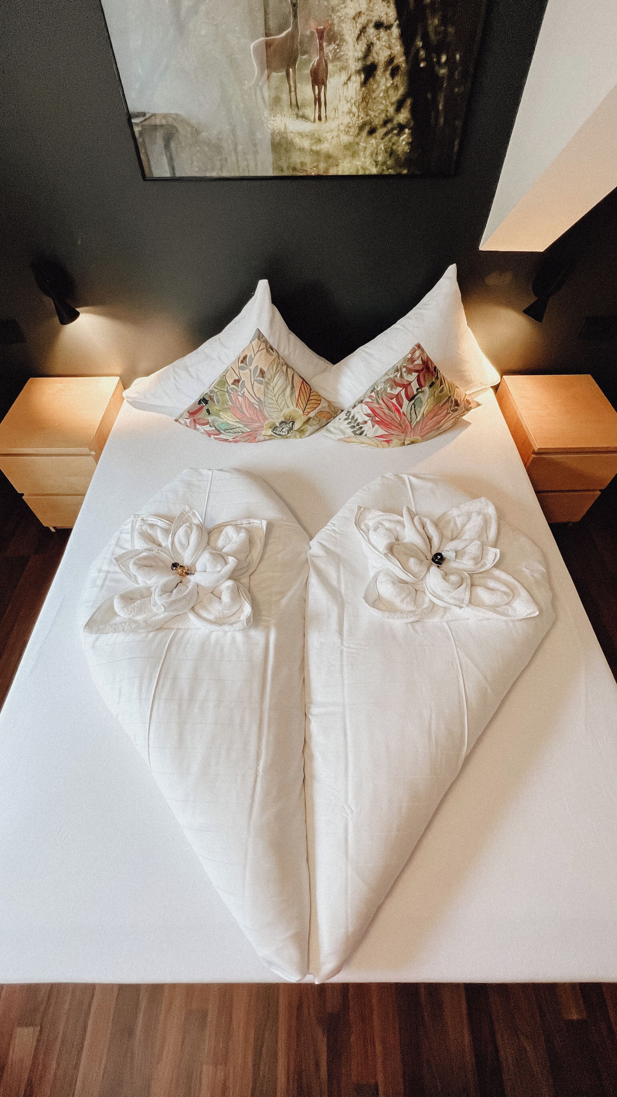 Een keurig opgemaakt bed met hartvormige kussens en een bloemenkussen.