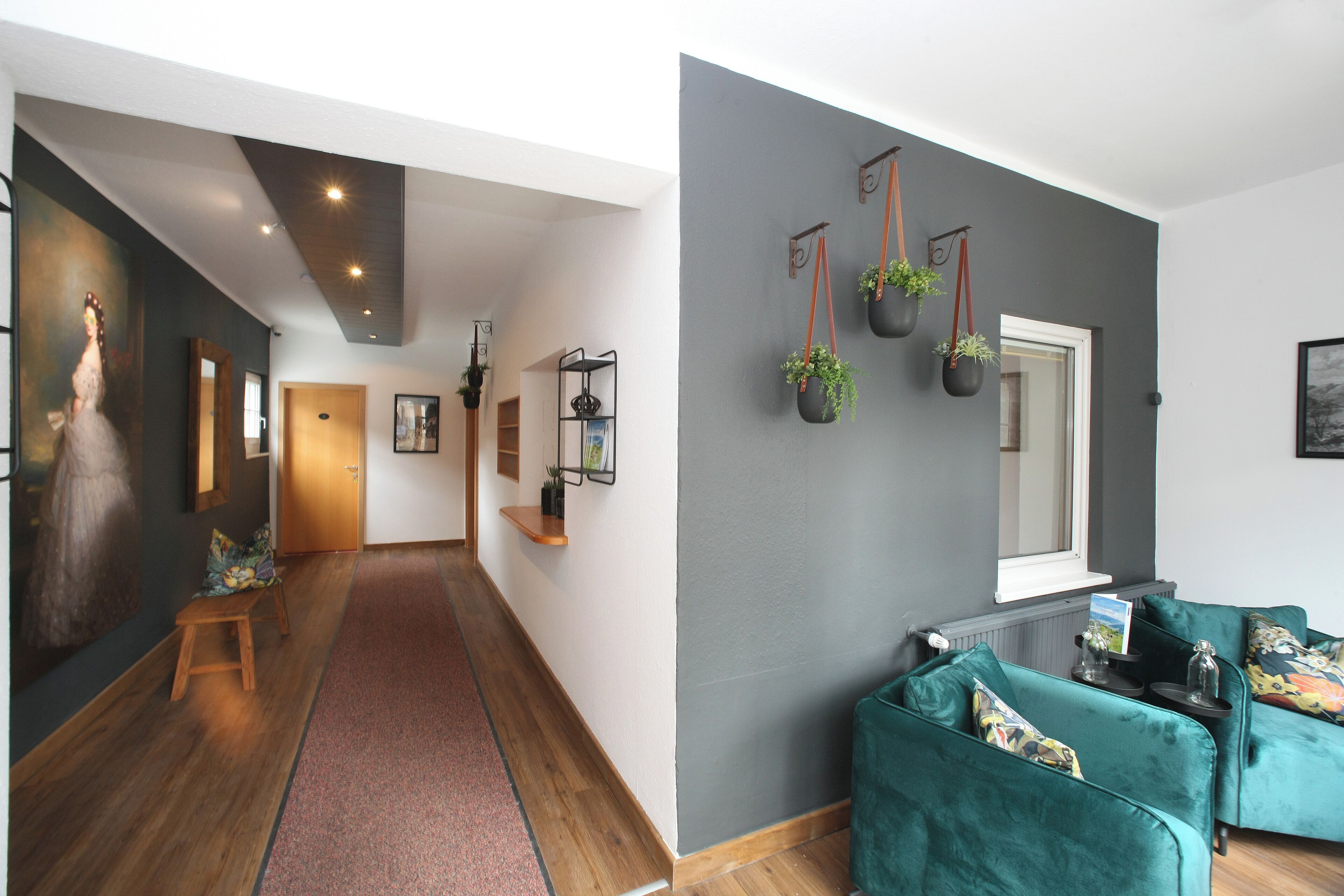Um interior moderno com um corredor de madeira, um conjunto de sofá verde e vasos de plantas fixados na parede.