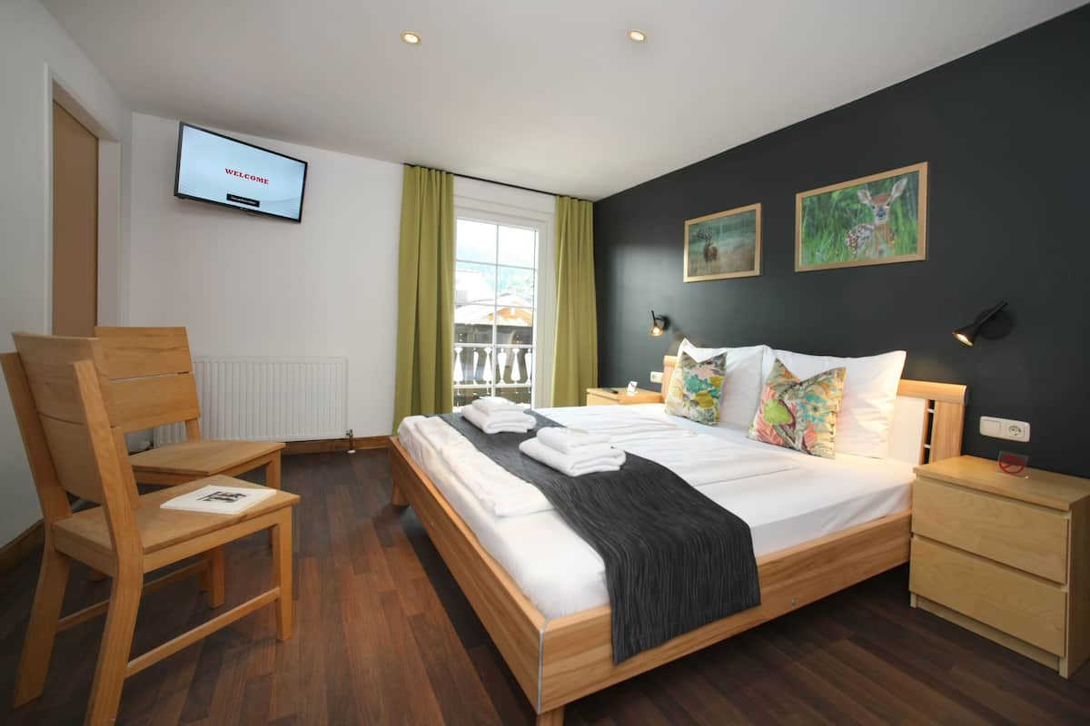 A modern hotel room with a large bed, wooden furniture, a TV on the wall, and artwork on the walls.