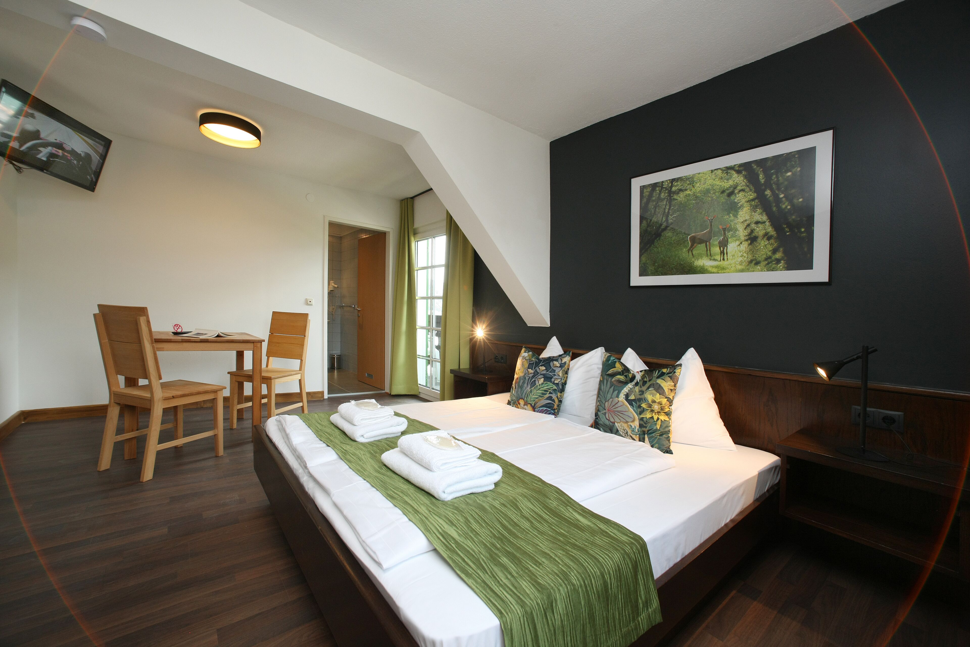 Een hotelkamer met een groot bed, een bureau met stoelen, een televisie en een lijst aan de muur.