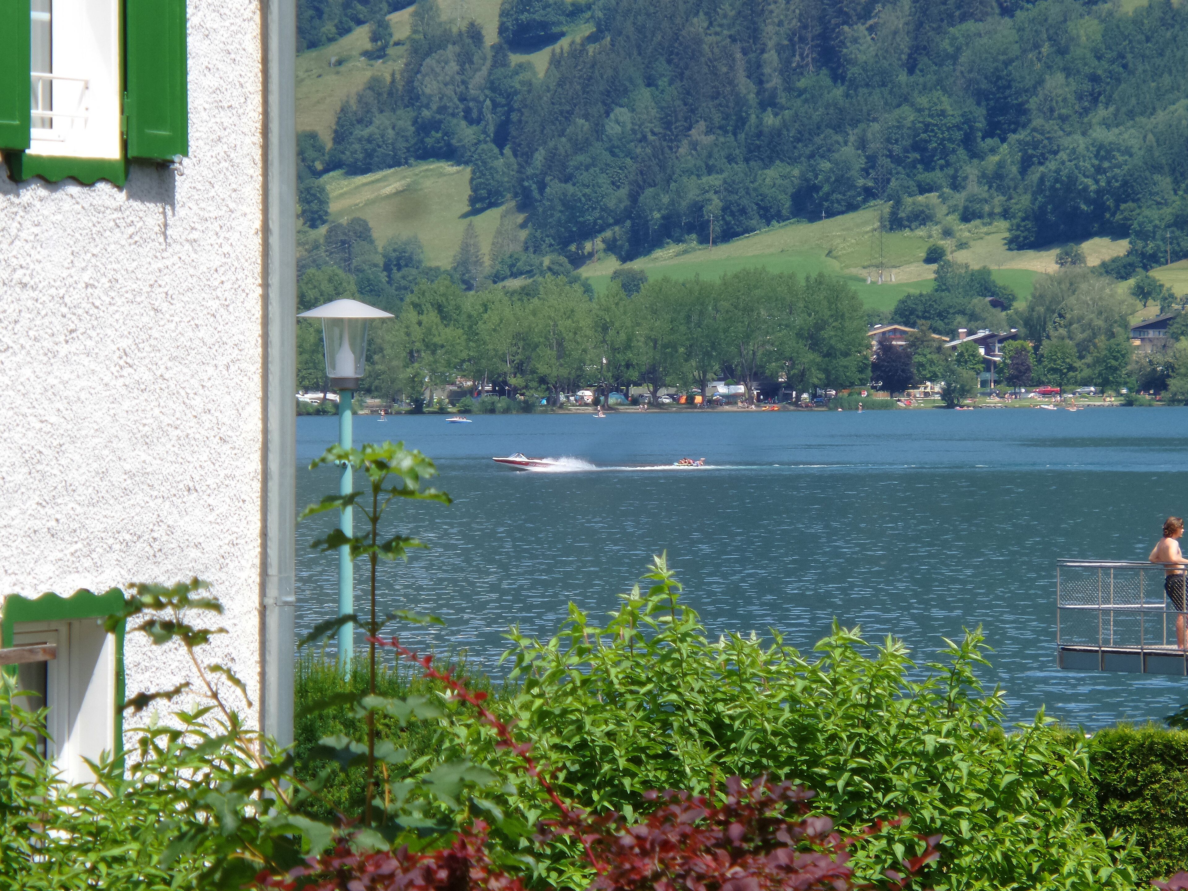 A lakeside view with a boat speeding across the water, a woman on a dock, and a building with a green door.